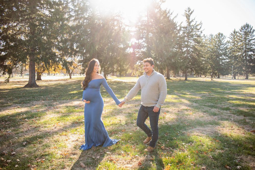 Couple enjoying moment together during outdoor maternity shoot with evergreen backdrop.