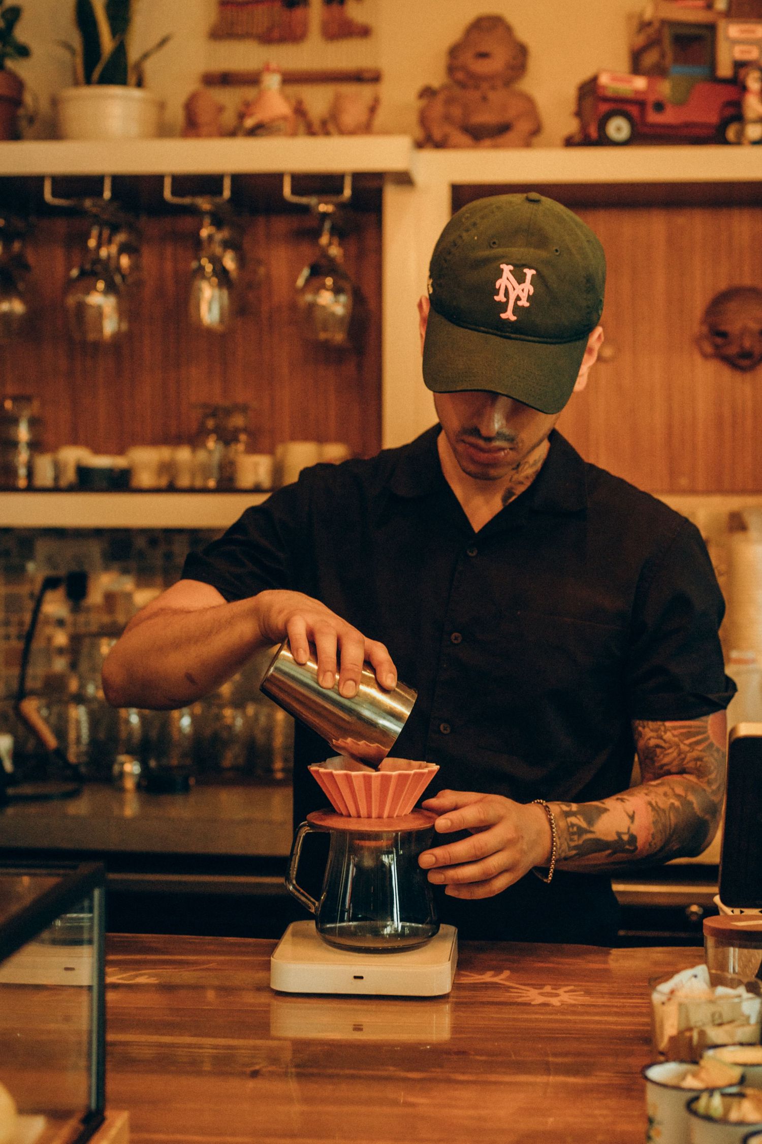 Barista preparing pour-over coffee using red filter in rustic cafe setting.