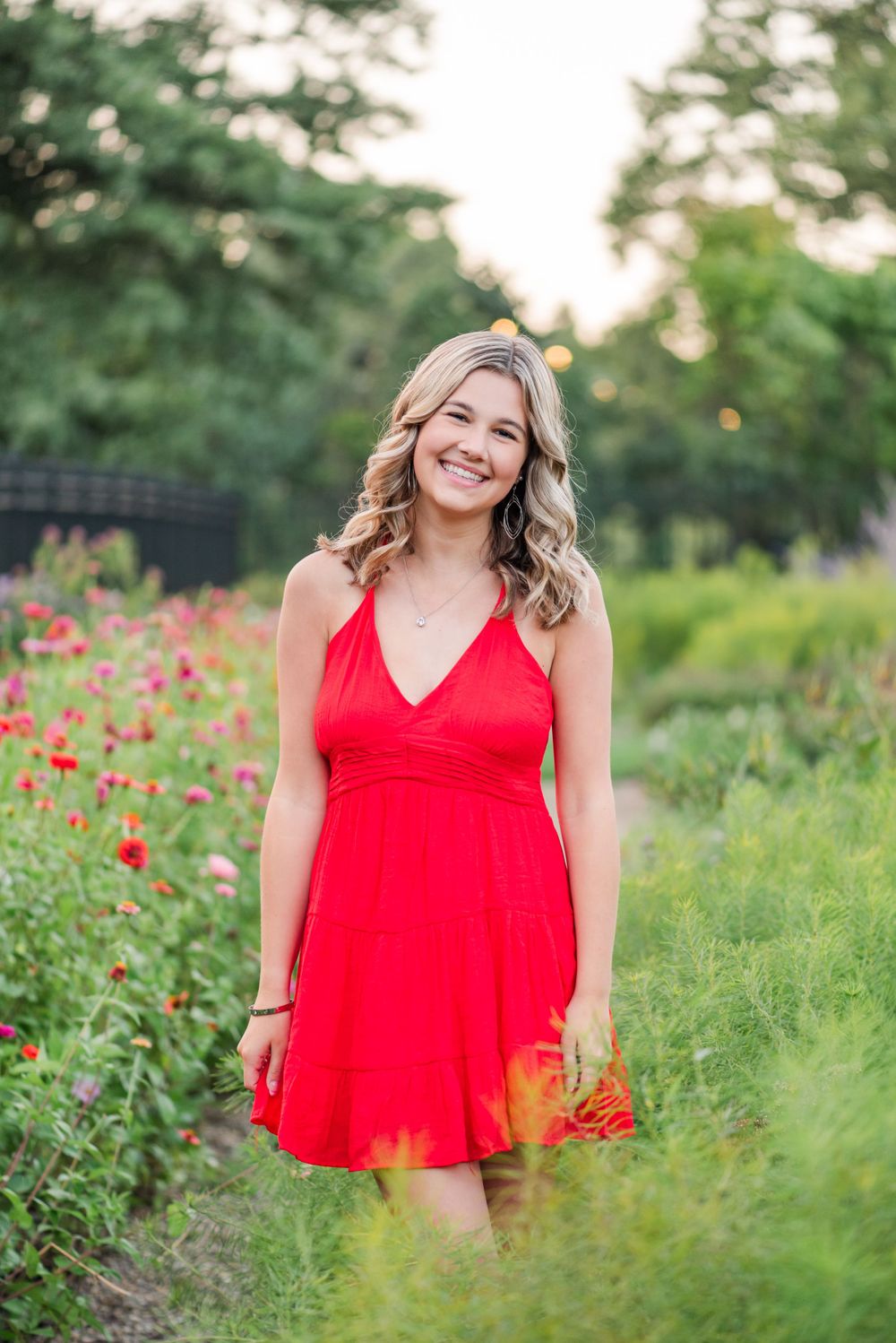 Summer portrait in red dress among wildflowers and garden greenery at sunset.