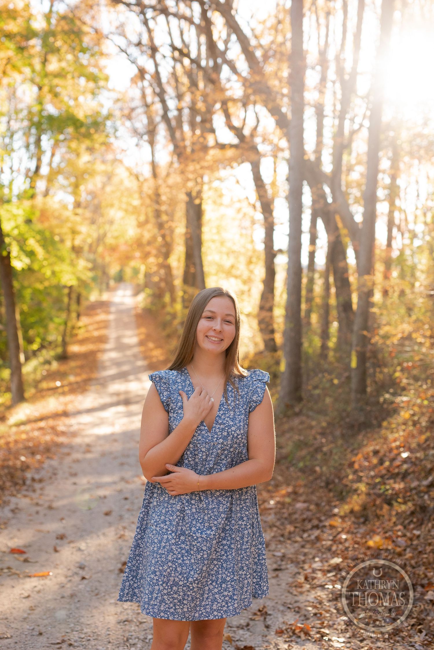 Sunlit forest path with golden leaves creating a warm backdrop for a blue dress portrait.