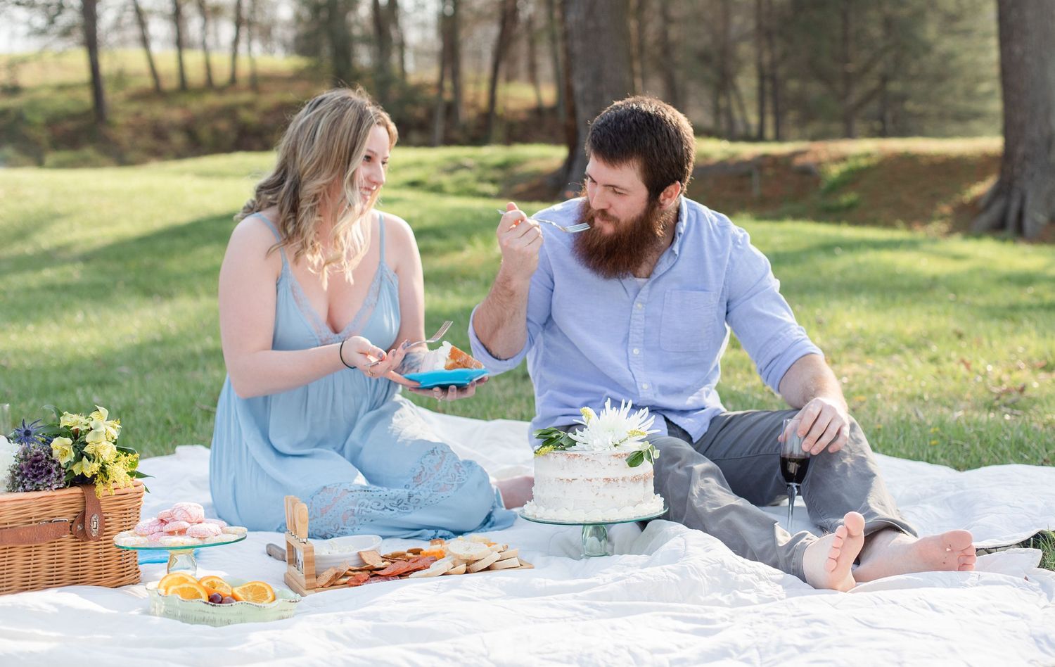 Scenic outdoor picnic spread with food and blanket on grassy lawn.