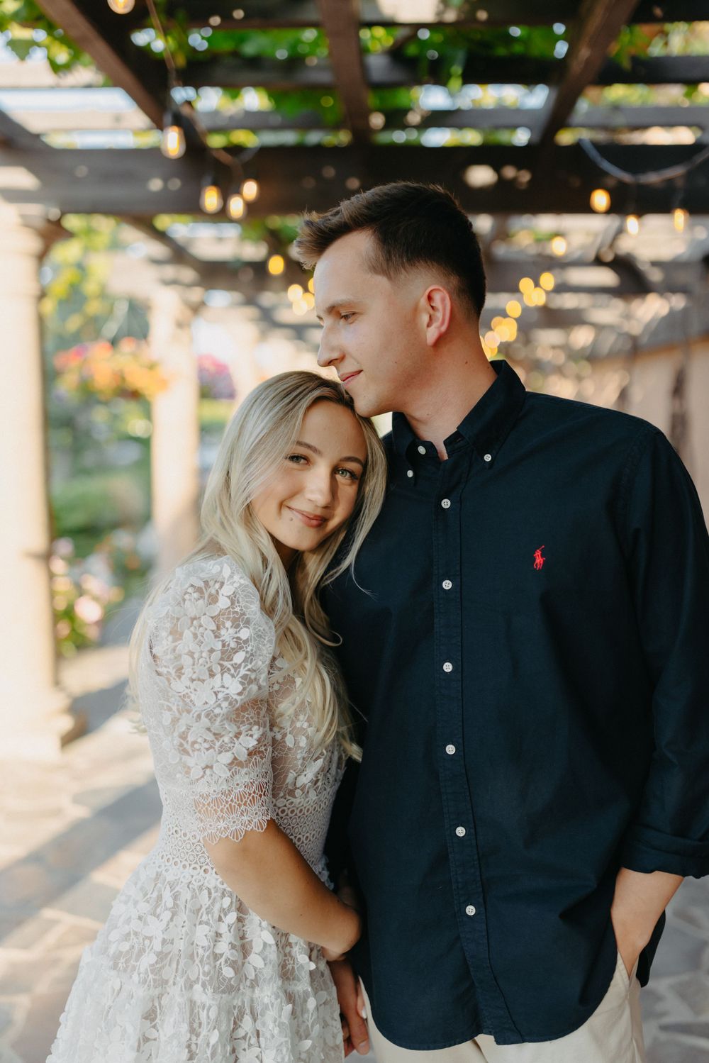 A romantic couple sharing an intimate moment under a pergola with twinkling lights.