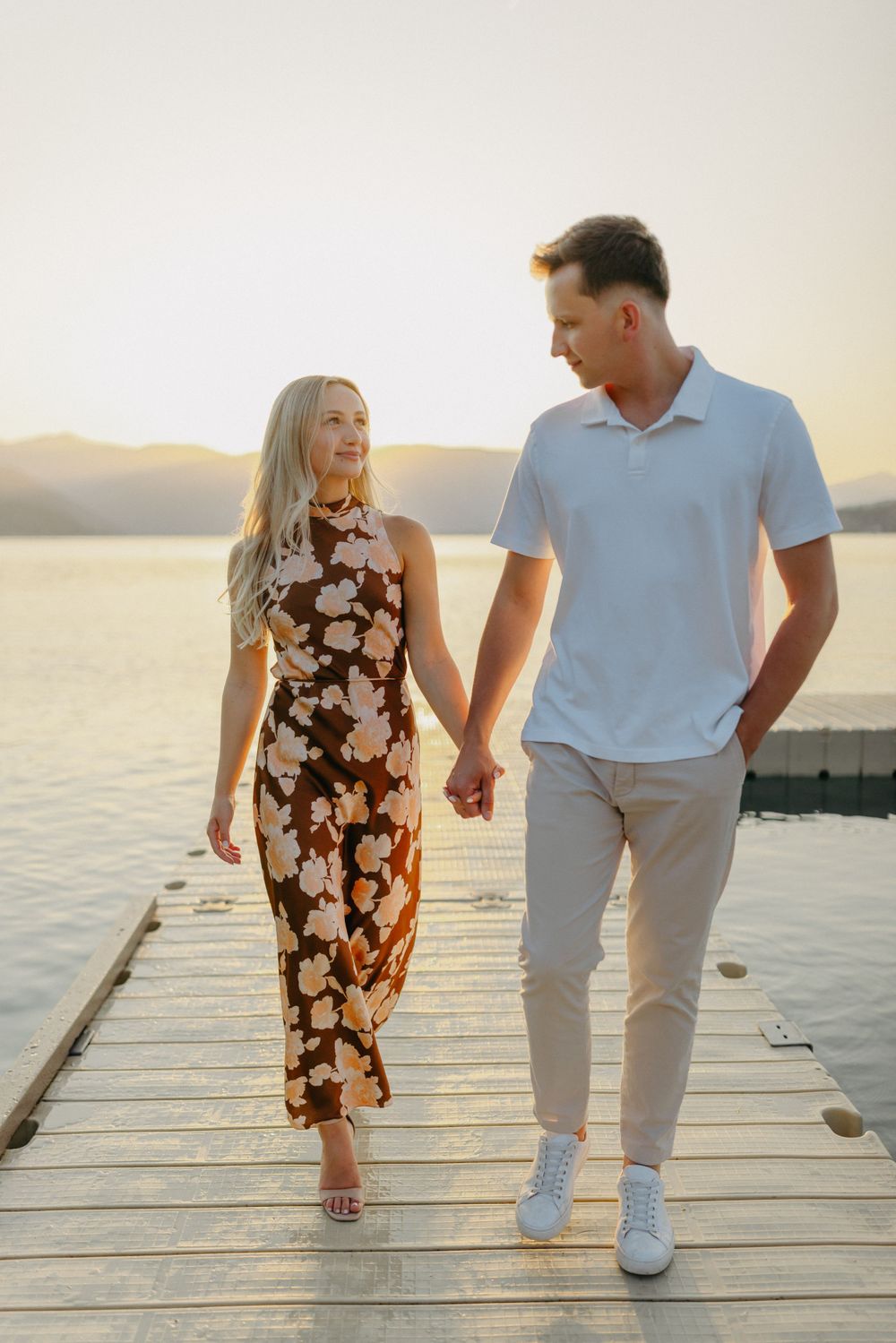 A couple walking hand in hand on a wooden dock at sunset wearing coordinated summer outfits.