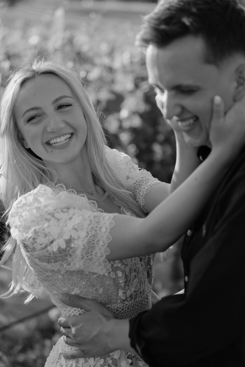 A black and white photo capturing an intimate moment between a couple in a vineyard setting.