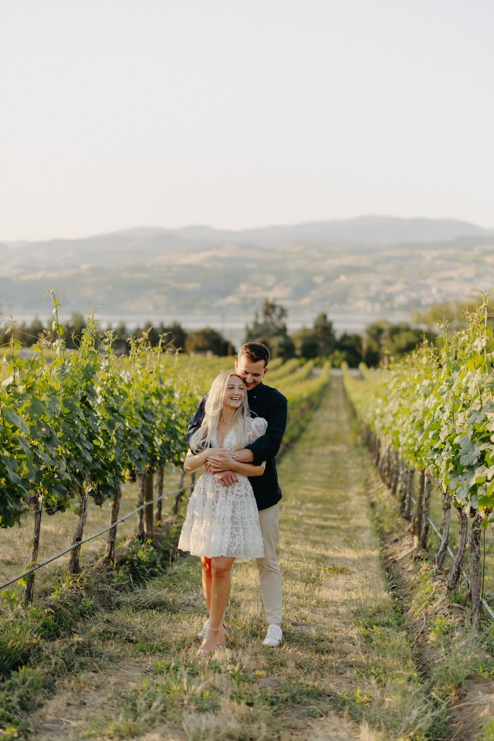 A romantic moment in a sun-drenched vineyard with rolling hills in the background.