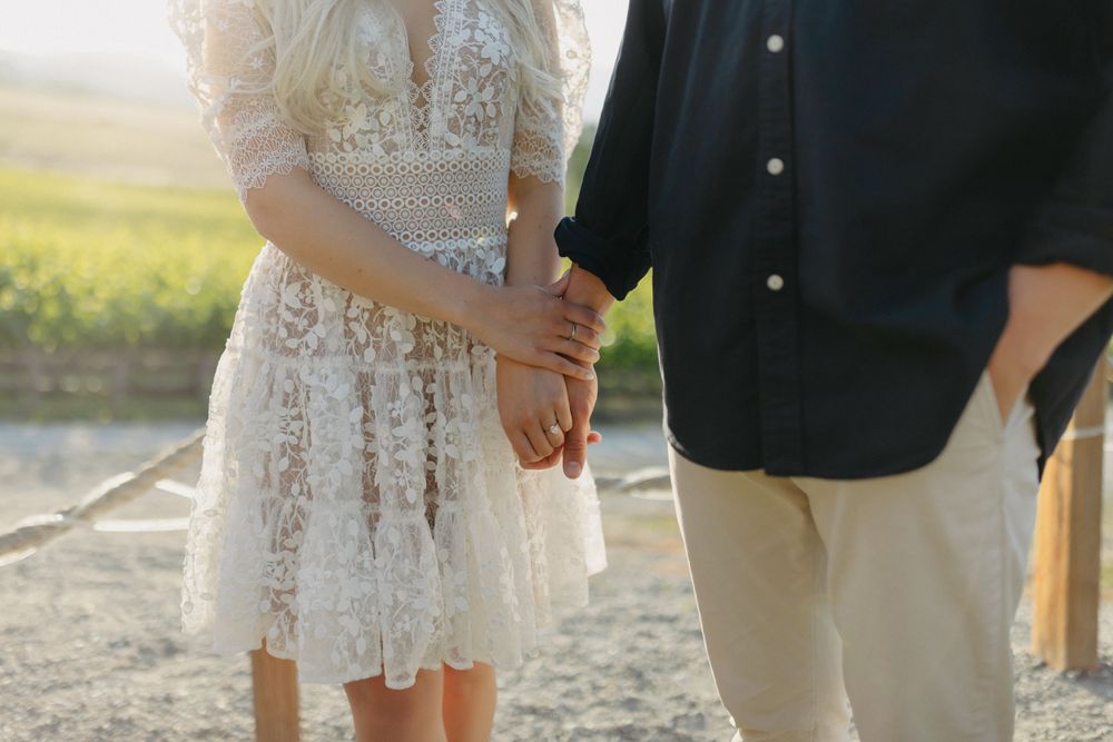 Close-up of a couple holding hands, showing white lace dress and dark shirt details.