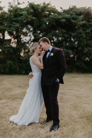 A romantic portrait of newlyweds embracing in a field at golden hour.