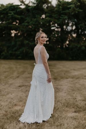 A bride in a fitted lace gown poses in a field at sunset.