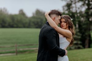 A romantic embrace between newlyweds in a pastoral setting.