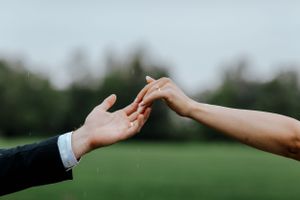 Two hands reaching toward each other against a blurred green background.