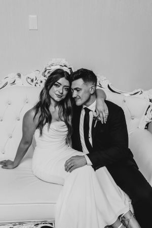 Black and white portrait of newlyweds sharing an intimate moment on an ornate white couch.