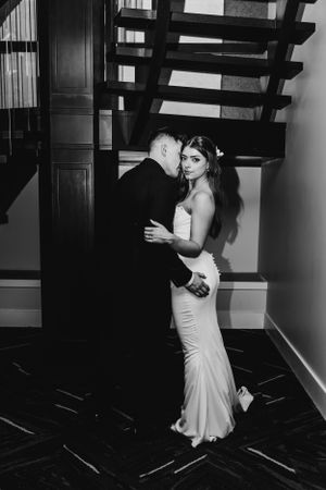 Romantic black and white photo of couple embracing near a modern staircase.