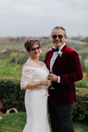 Couple in wedding attire toasting with champagne glasses in garden setting.
