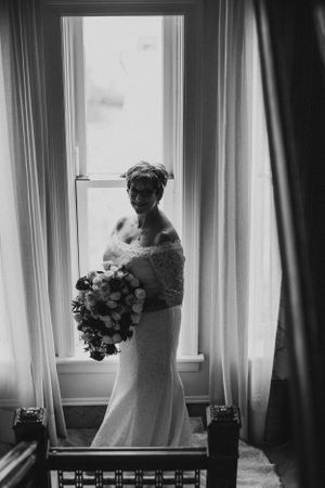Black and white silhouette of bride holding bouquet while standing by window.