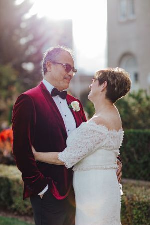 Elegant couple in burgundy and white wedding attire sharing tender moment outdoors.