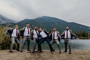 Groomsmen in matching outfits striking fun poses by mountain lake.