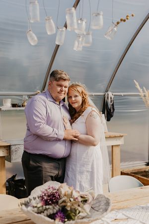 Couple embracing in greenhouse with hanging mason jar lights and rustic decor.