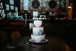 Elegant three-tier marble-effect wedding cake on dark wooden table in rustic venue.
