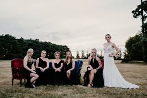 Wedding party poses on vintage furniture outdoors with bridesmaids in black dresses.