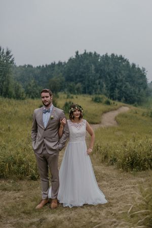 A newlywed couple poses on a rustic trail with natural greenery and trees in the background.