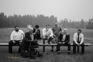 A group of people sitting casually on a wooden bench in a black and white outdoor photograph.
