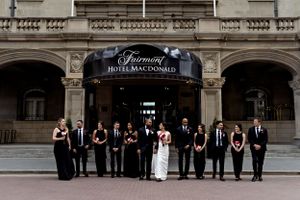 Wedding party in formal attire poses outside historic Fairmont hotel entrance.