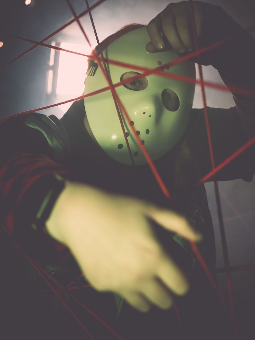 Spooky green hockey mask emerging from shadows with red string accents.