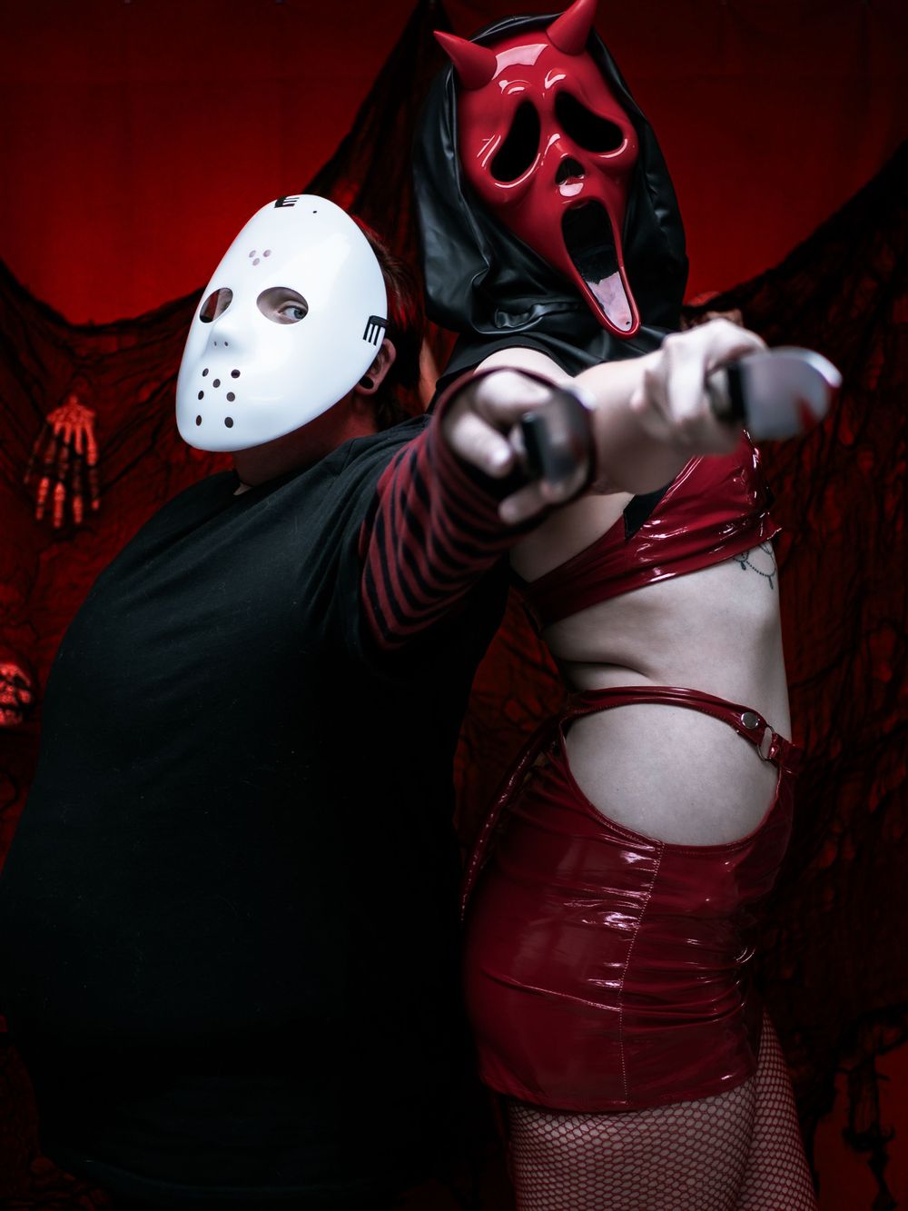 Dramatic pose of two masked figures in horror costumes against red background.