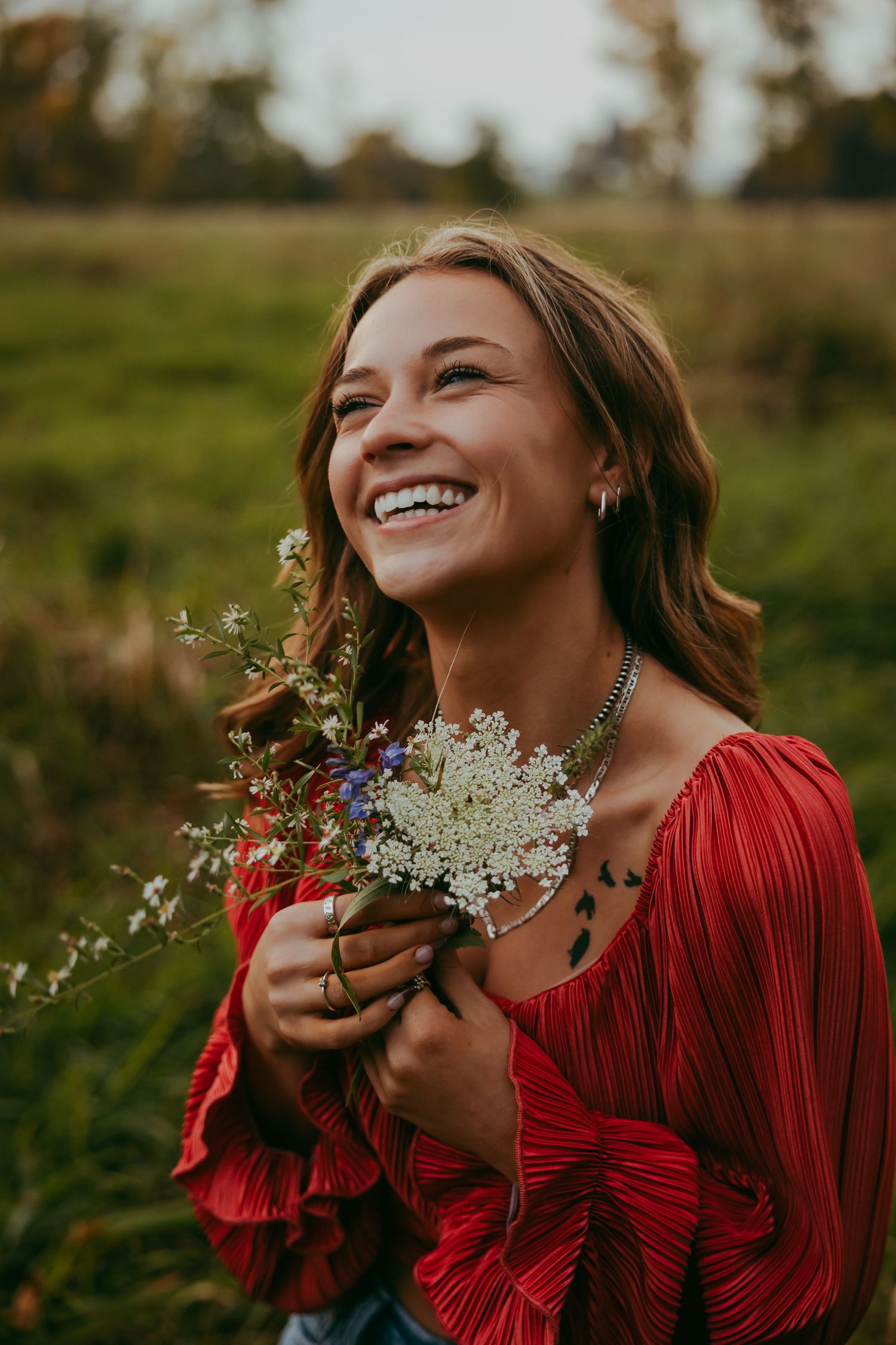 Woman in red dress laughs while holding wildflowers in sunlit field.