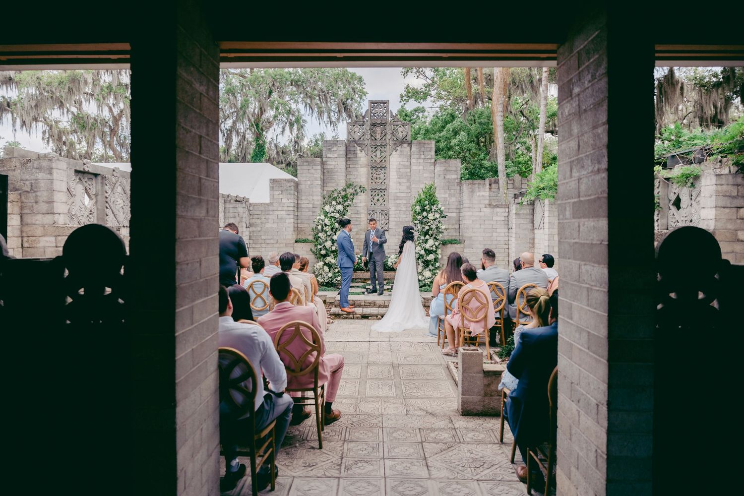 Wedding ceremony taking place in an elegant stone courtyard with guests seated on either side of the aisle.