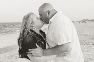Black and white photo of a couple kissing on the beach with ocean in background.
