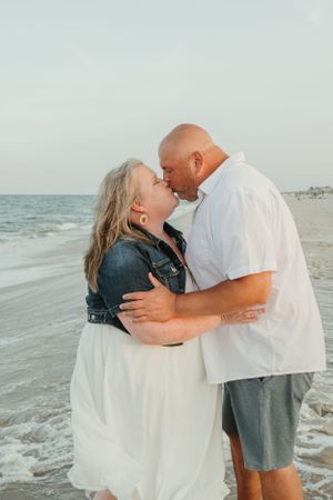 Romantic couple embracing and laughing together on a sunny beach with ocean waves in background.
