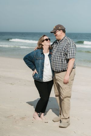 Playful couple enjoying a romantic moment on a sunny beach with waves crashing behind them.