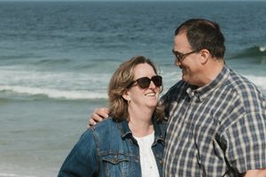 Happy couple walking and laughing together along a beach shoreline on a bright day.