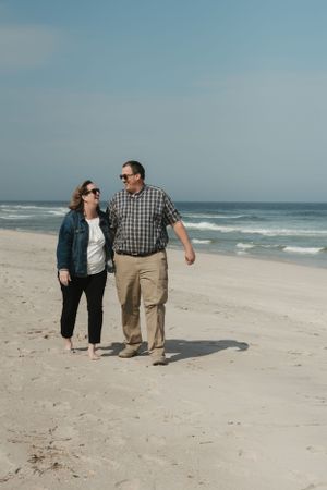 Couple strolling together on empty sandy beach with waves and ocean in background.