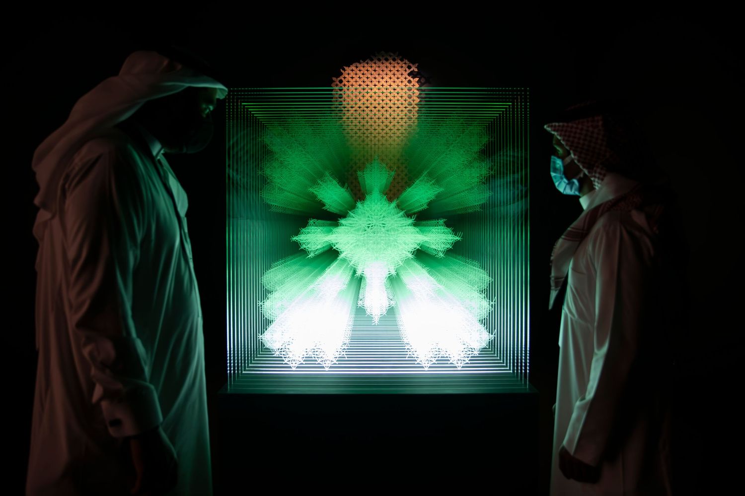 A green illuminated art piece creates geometric patterns between two viewing figures.