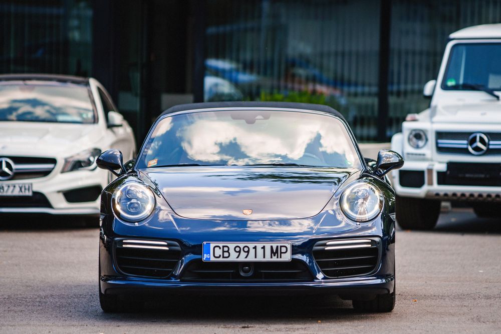 Front view of a blue Porsche 911 sports car parked between Mercedes vehicles.
