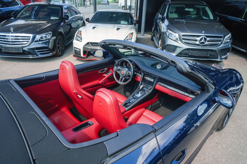 Convertible Porsche 911 interior with striking red leather upholstery and modern dashboard controls.