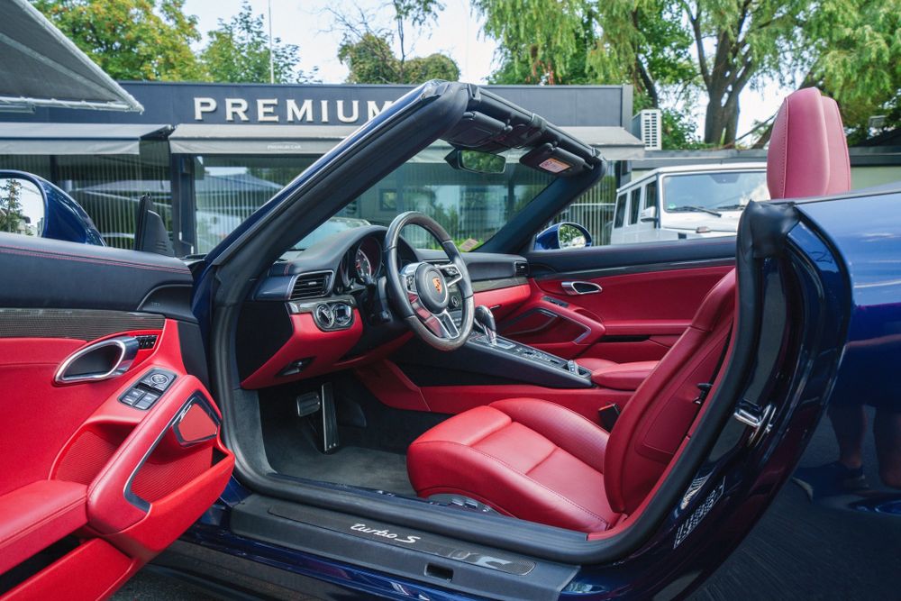Open door view of a Porsche 911's red leather interior and sport steering wheel.