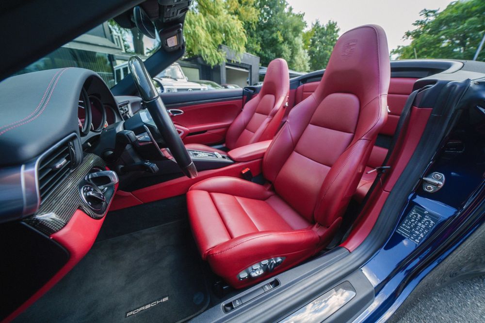 Driver's side interior view of red leather seats and black dashboard in a Porsche 911.