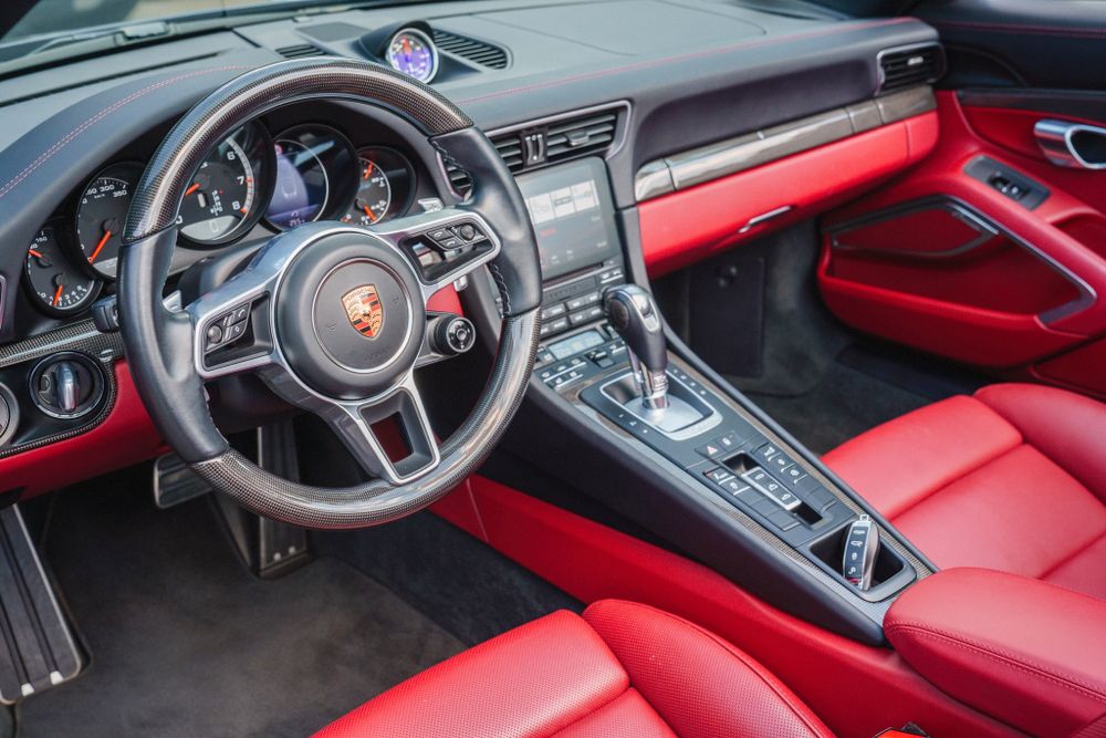 Porsche 911 dashboard with leather-wrapped steering wheel and red interior trim.