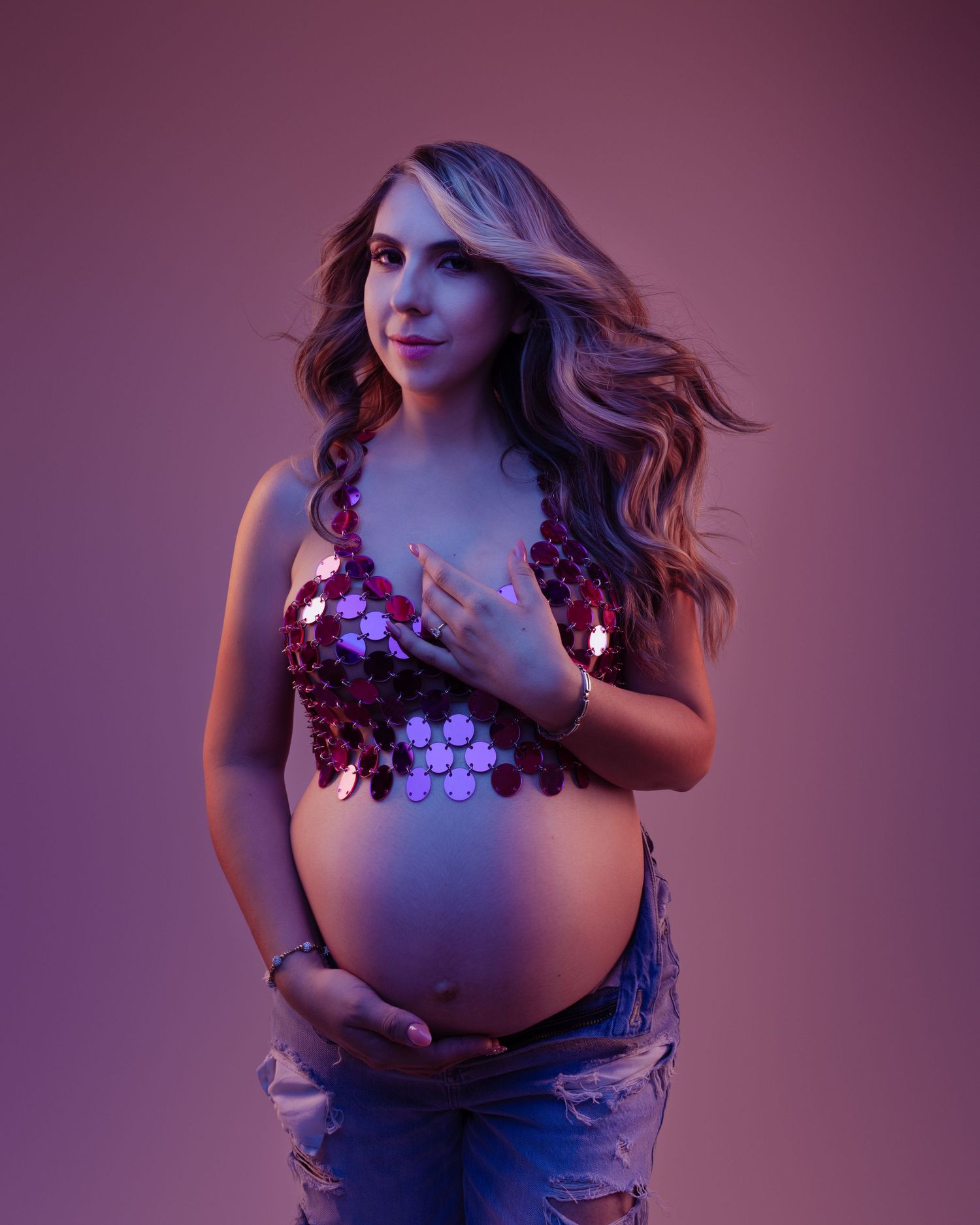 Modern maternity portrait with purple sequin top and denim in moody lighting.