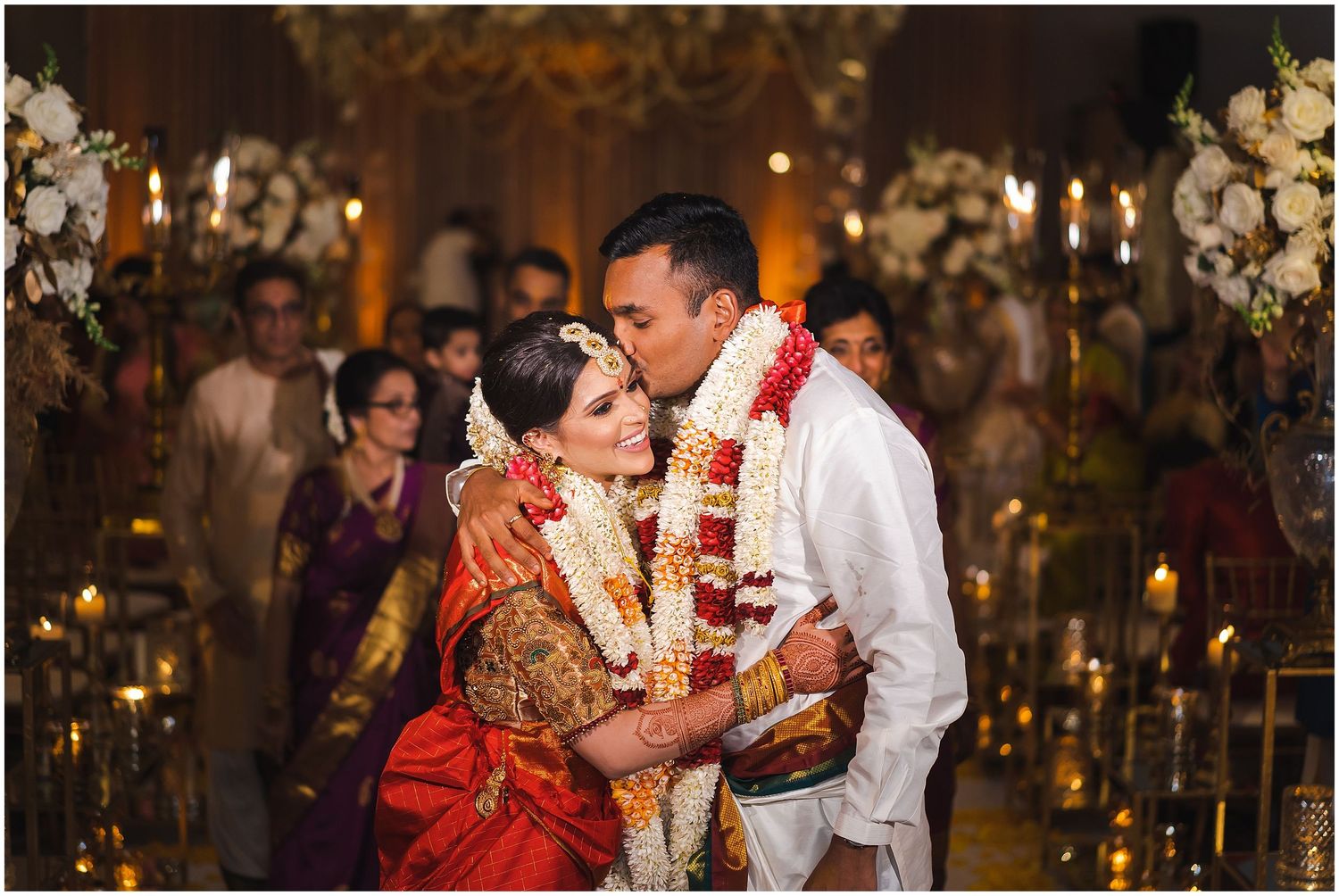 Romantic candlelit wedding ceremony in an ornate venue decorated with white floral arrangements.