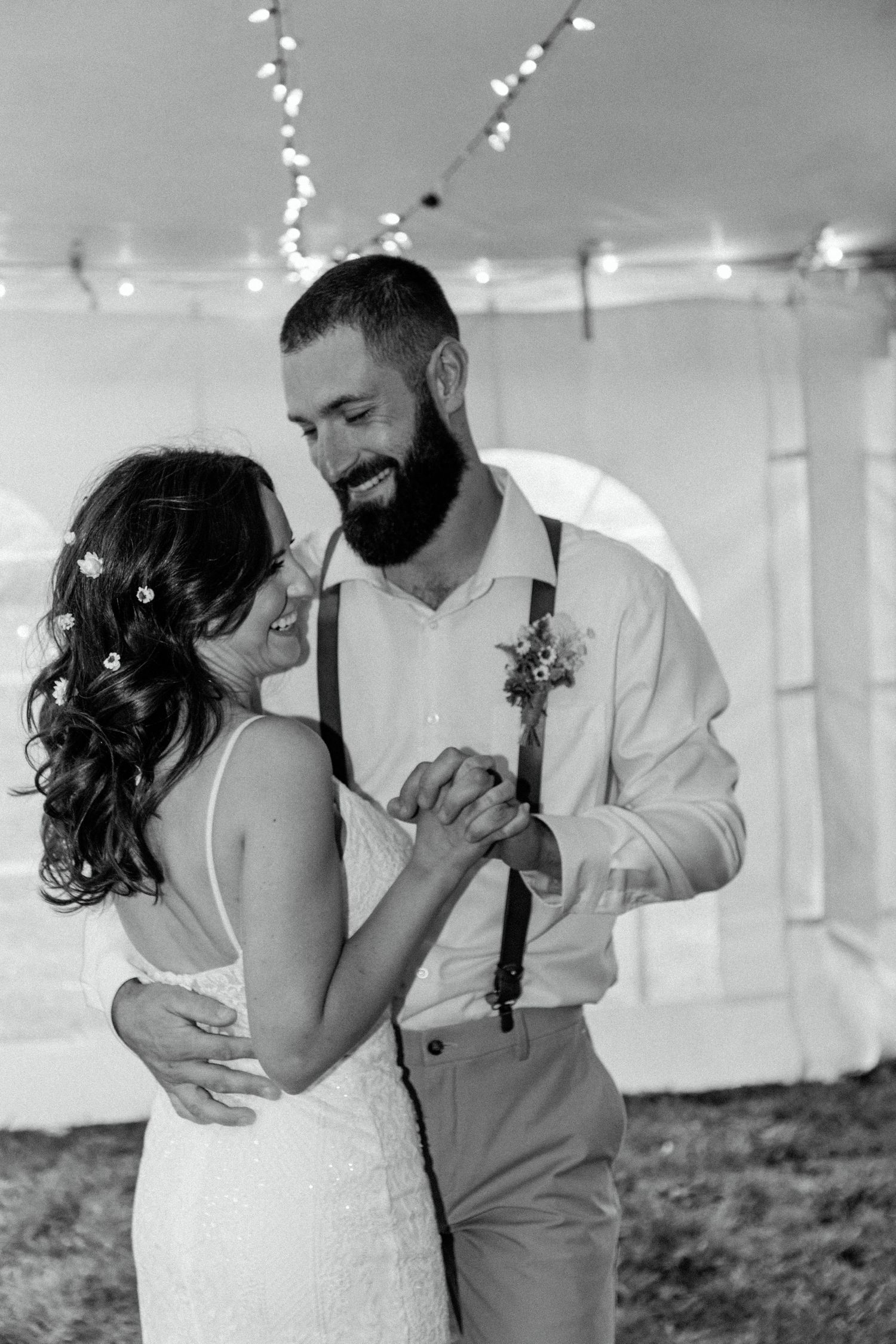 A tender black and white dance moment between newlyweds under string lights.