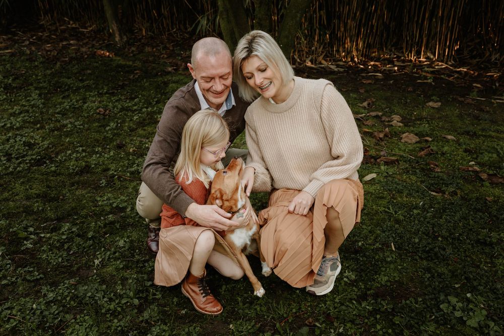 A family group sits together on grass with their golden retriever in soft autumn light.