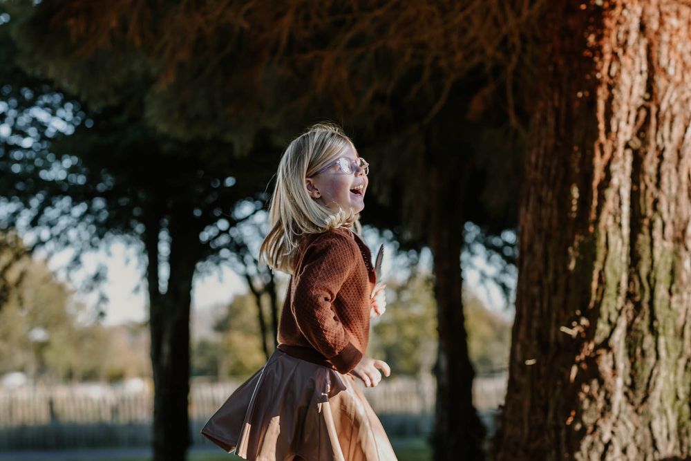 A whimsical autumn scene of dancing and twirling in a park among tall trees.