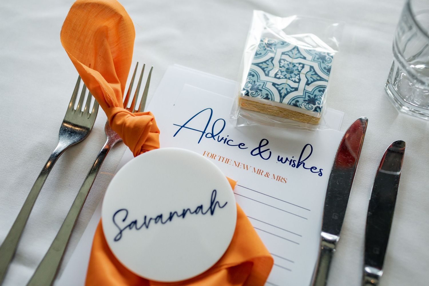 Place setting with orange napkin, personalized plate, and favor box in blue and white pattern.