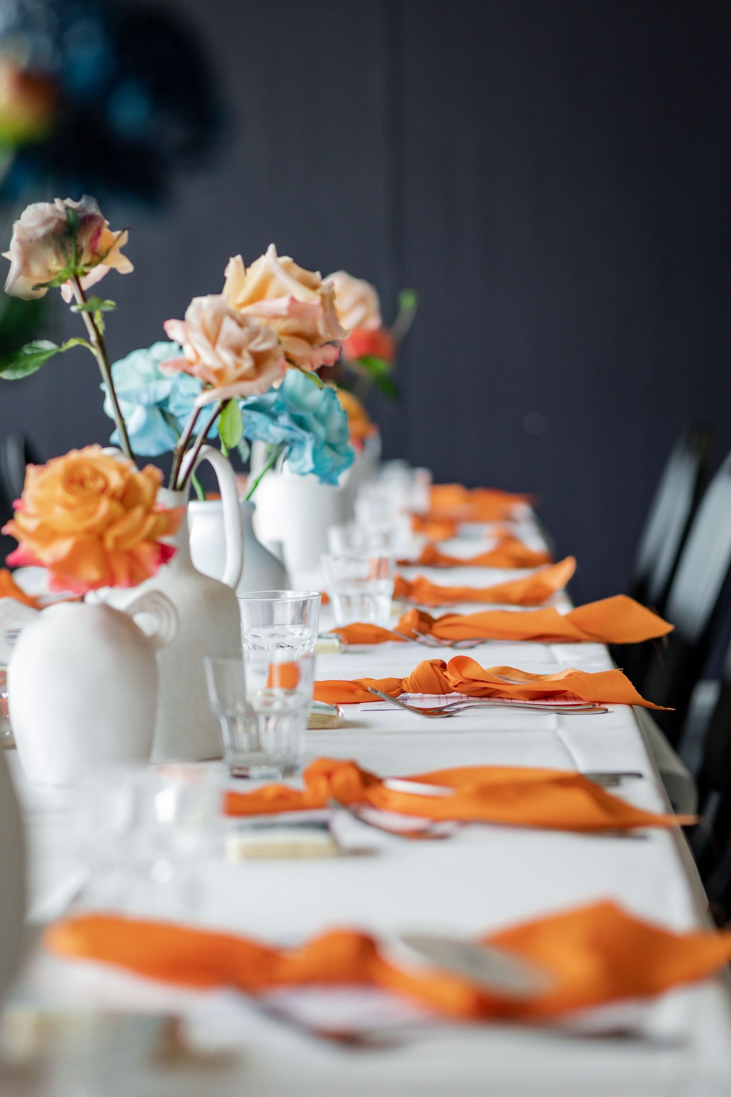 Elegant table setting with orange napkins and peach and blue floral centerpieces.