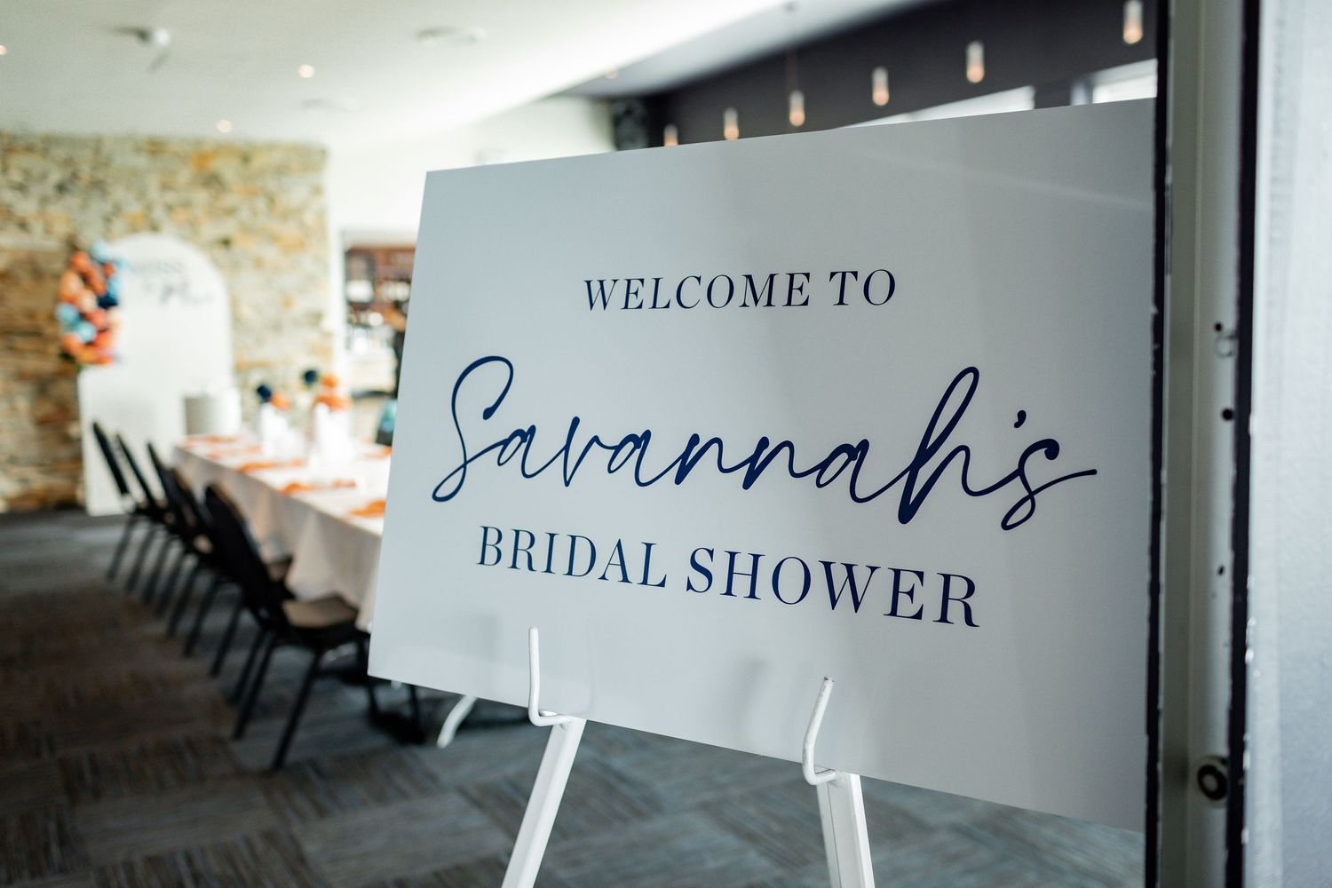 Welcome sign for Savannah's bridal shower displayed on a white easel in an industrial venue.