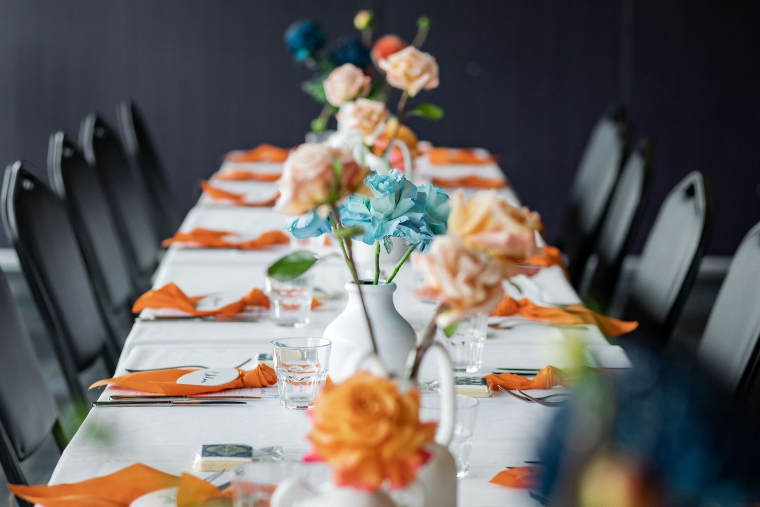 Elegant table setting with orange accents and blue floral centerpieces in modern restaurant space.